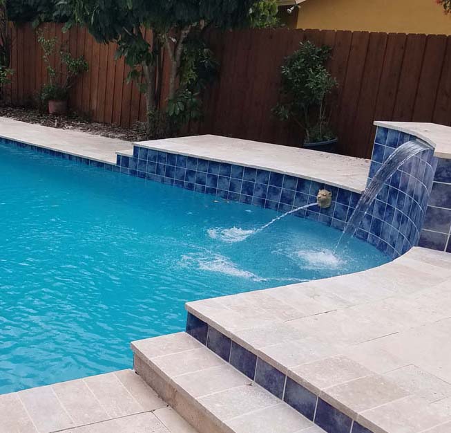 A backyard pool with a blue waterfall feature and tiled edges.